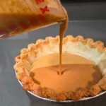 pouring pumpkin pie filling into a pie shell