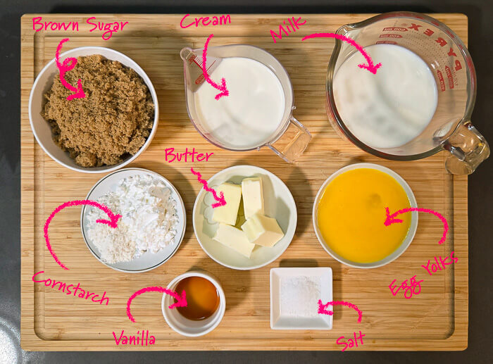 ingredients for butterscotch pie laid out on a cutting board: brown sugar, heavy cream, whole milk, butter, cornstarch, vanilla extract, salt, and egg yolks