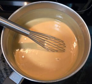 a photo of a pot with a whisk and butterscotch custard after cooking
