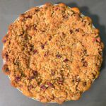 a beautiful baked caramel apple pie topped with a pecan crumble in a crimped pie crust