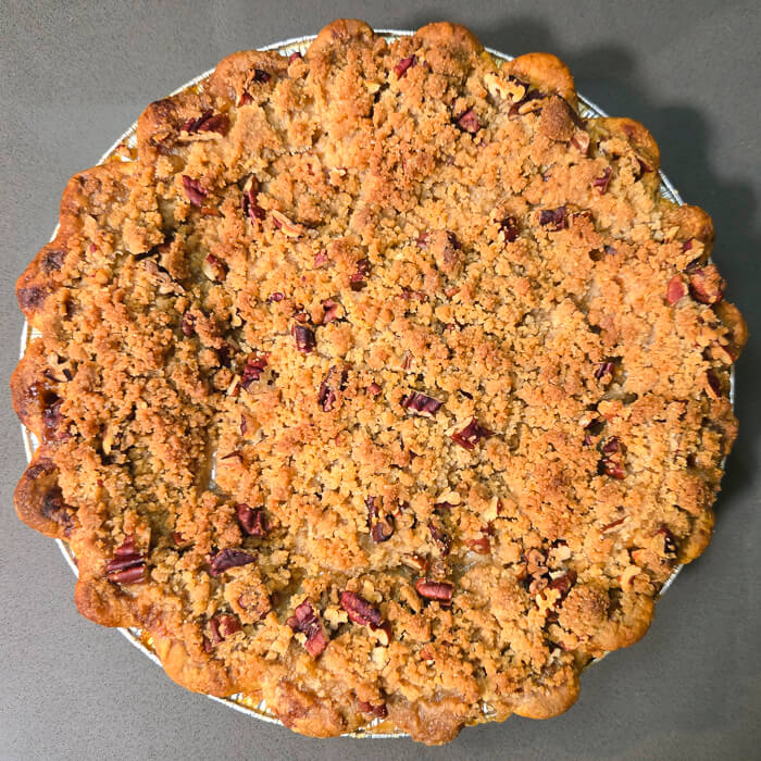 a beautiful baked caramel apple pie topped with a pecan crumble in a crimped pie crust
