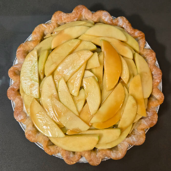 a pie shell with unbaked caramel apple pie filling inside and the edges of the pie crust creamed, almost ready to go in the oven