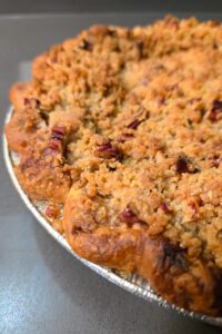 a close up shot of a baked caramel apple pie with pecan crumble topping