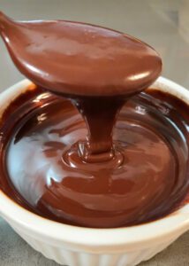 close up photo of chocolate ganache recipe coming off of a spoon and falling into a bowl in smooth ribbons