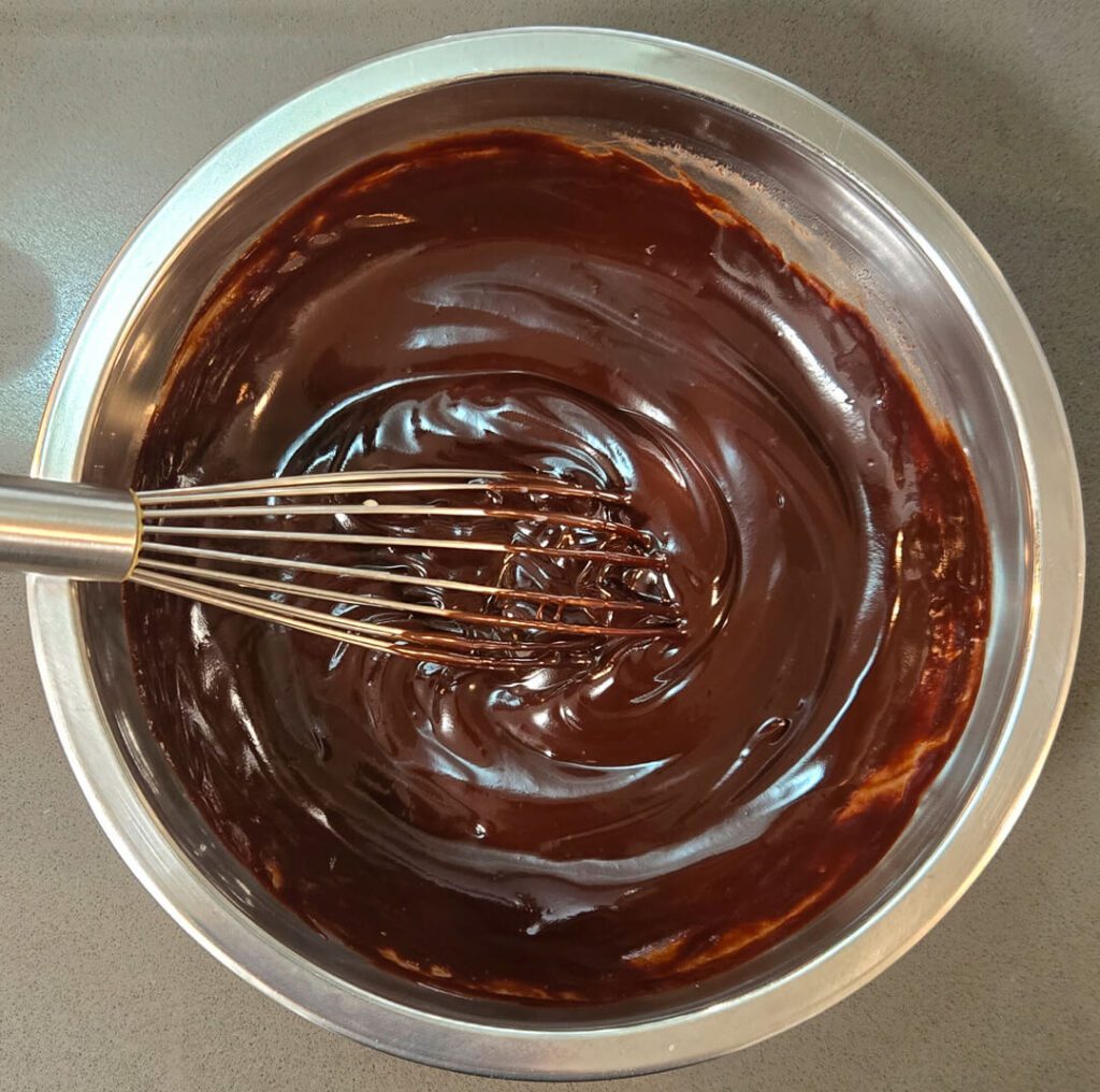freshly mixed chocolate ganache in a metal mixing bowl with a whisk