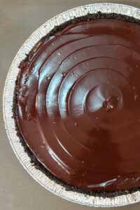 close up overhead shot of half of a peanut butter pie recipe with glossy chocolate ganache and an oreo pie crust