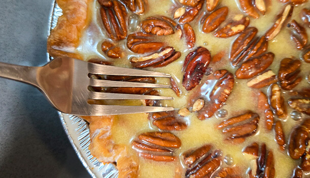 close up shot of using a fork to dunk toasted pecans in pecan pie filling so they don't burn