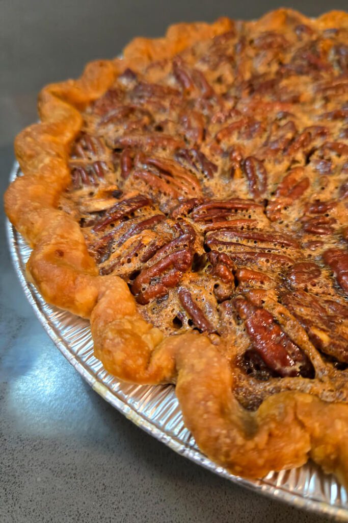close up shot of a baked pecan pie recipe with a golden brown buttery pie crust and candied pecans