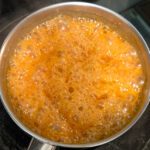 a photo of a pot with cream being added to hot caramel causing sizzling and bubbling