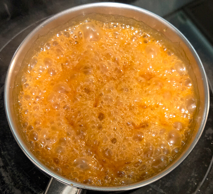 a photo of a pot with cream being added to hot caramel causing sizzling and bubbling