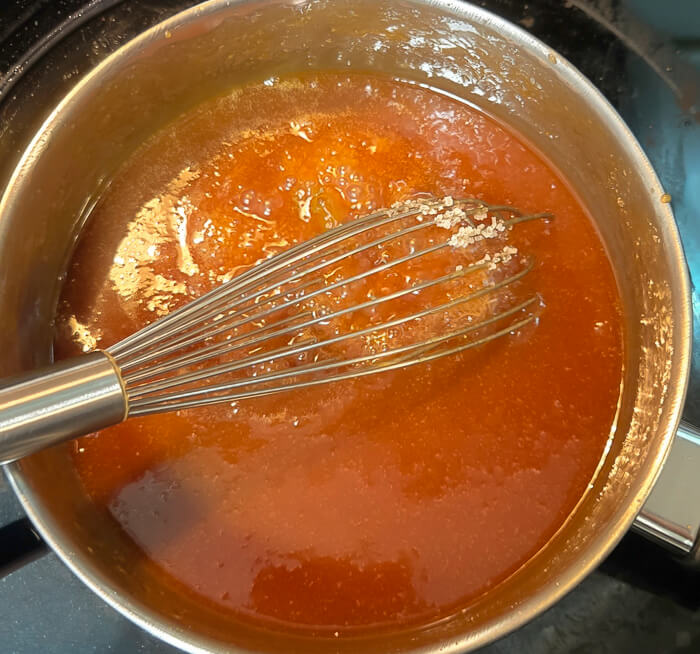 a photo of a pot with a whisk in it of caramel sauce