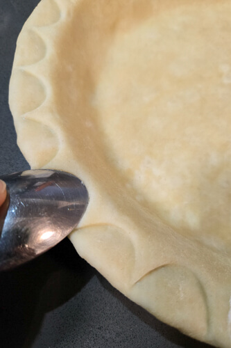 using a spoon to decorate the edge of a pie crust