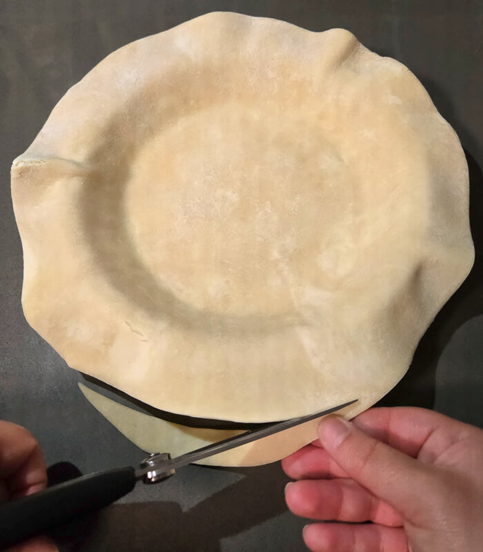 trimming a pie crust fitted into a pie tin