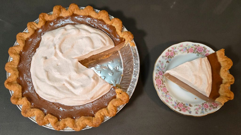 overhead photo of an apple butter pie with a slice cut out and placed on a floral plate next to the rest of the pie