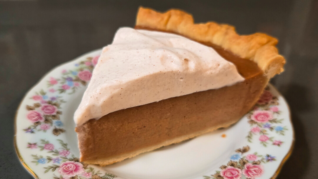 a close up photo of a slice of apple butter pie topped with cinnamon whipped cream on an antique floral plate