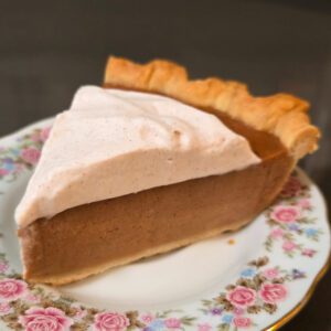 a close up square photo of a slice of apple butter pie topped with cinnamon whipped cream