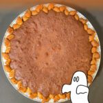 Whole brownie pie with orange gradient background and ghost graphic, labeled “Brownie Pie Recipe Perfect for Halloween,” fall dessert photo.