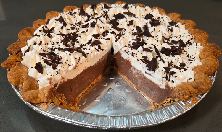 cross section photo of a chocolate cream pie with a slice cut out showing flaky crust, whipped cream and chocolate shavings, and rich chocolate pudding