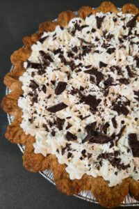 close up photo of a chocolate cream pie topped with piped whipped cream and chocolate shavings in a flaky pastry crust for chocolate cream pie recipe