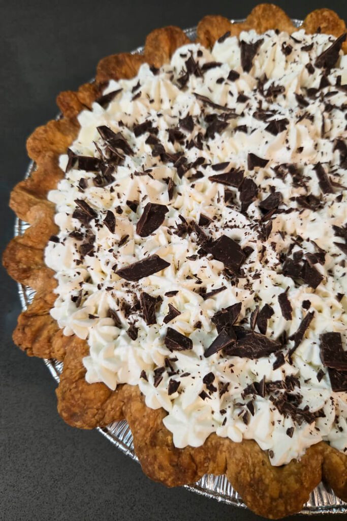 close up photo of a chocolate cream pie topped with piped whipped cream and chocolate shavings in a flaky pastry crust for chocolate cream pie recipe