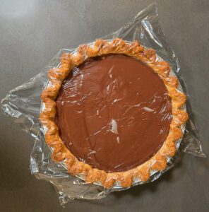 photo showing plastic wrap pressed over the top of freshly made chocolate pudding so it doesn't develop a skin as it cools