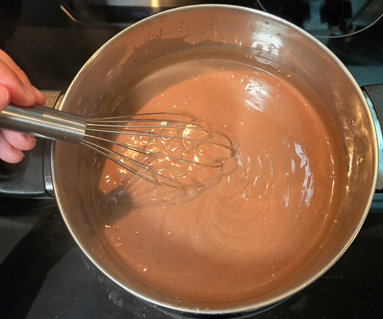 whisking chocolate pudding in a pot on the stovetop as it cooks