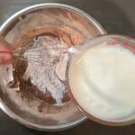 process photo showing how to temper eggs in chocolate pudding. Show chocolate pudding being whisked vigorously as a small amount of milk is poured in