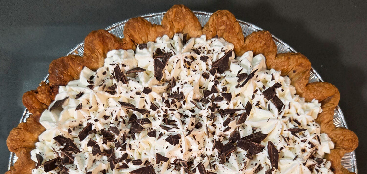 top half of a chocolate cream pie topped with decorative whipped cream, chocolate shavings
