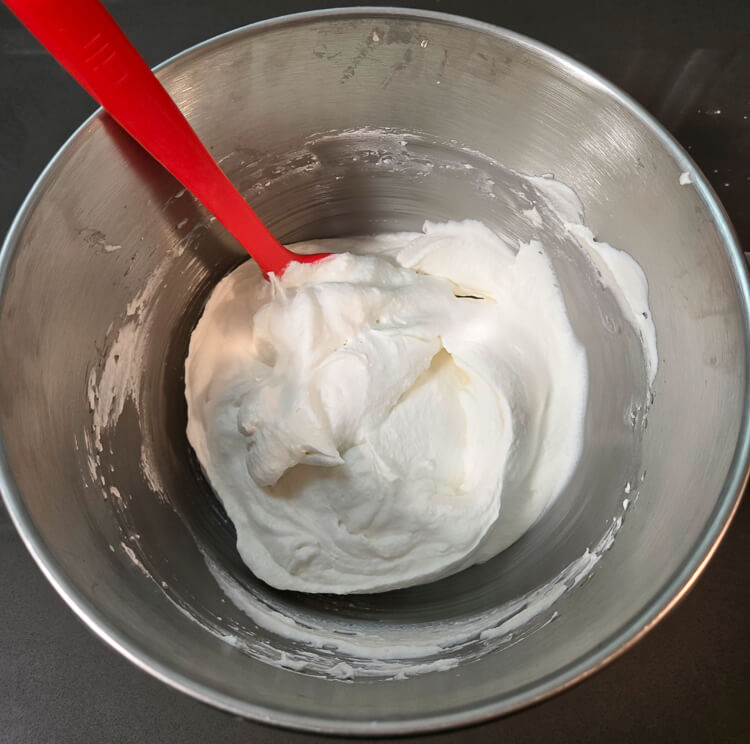 whipped cream in a mixing bowl with a red spatula