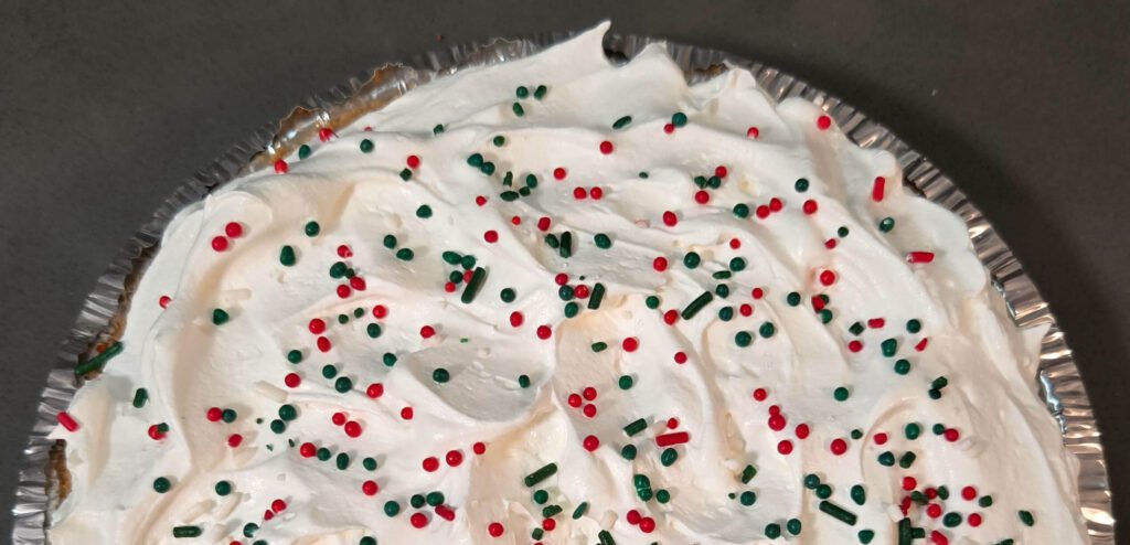 an overhead photo of half of a pie topped with whipped cream and christmas themed sprinkles
