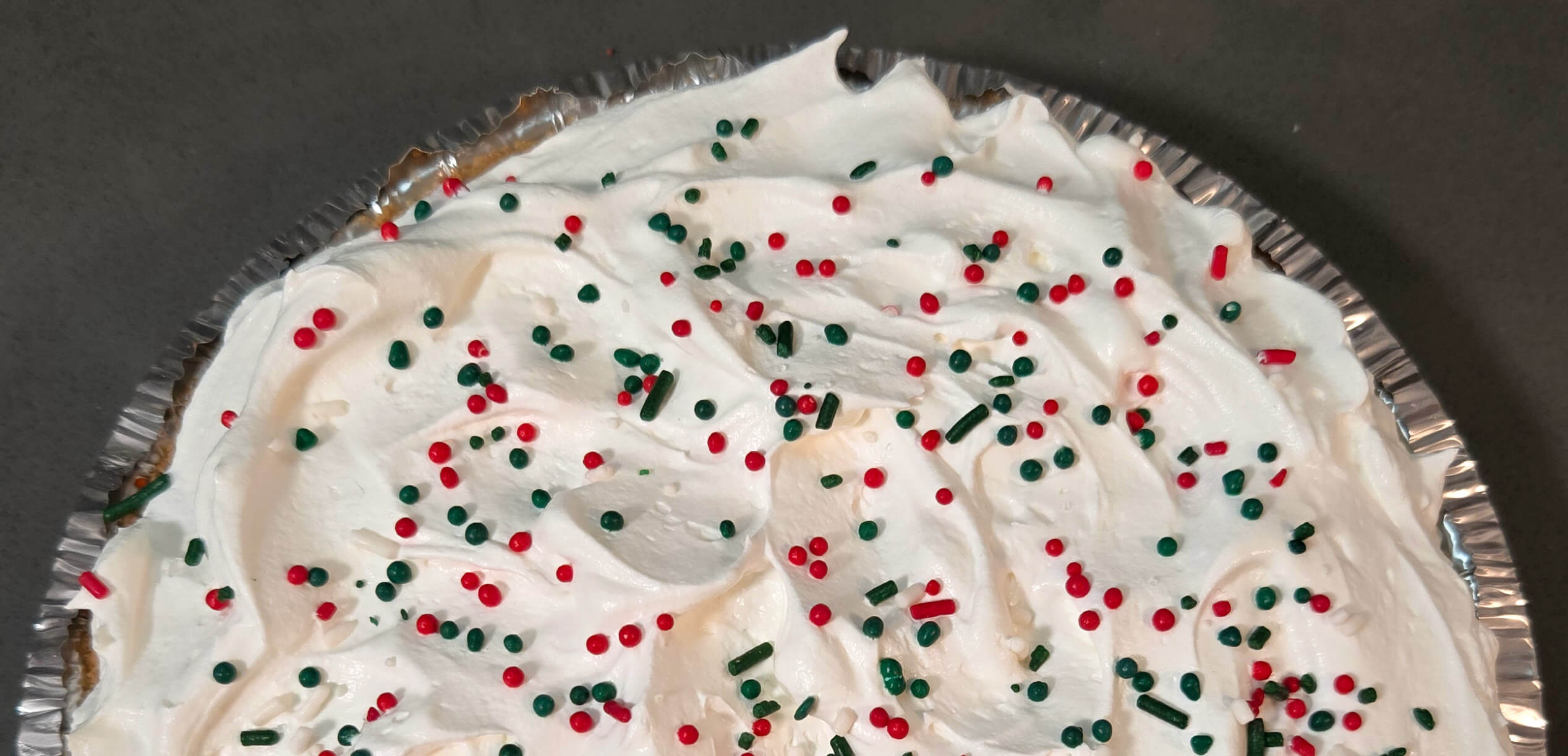 an overhead photo of half of a pie topped with whipped cream and christmas themed sprinkles