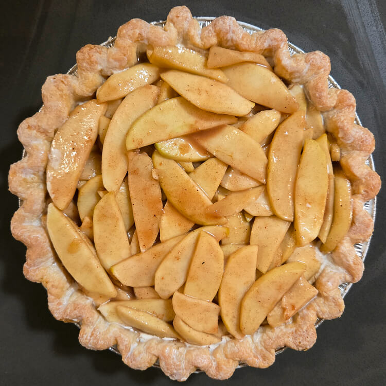 apple pie filling in a blind baked pie shell where the edges of the crust have been brushed with cream for baking