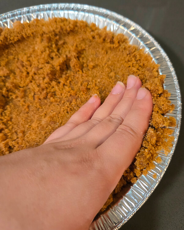 a photo of how to press a graham cracker crust into a pie tin