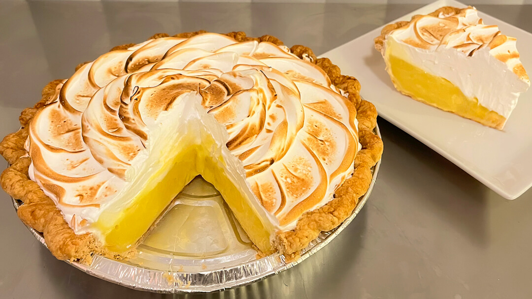 Lemon meringue pie with toasted swirls of meringue topping and a slice on a white plate showing bright yellow lemon filling.