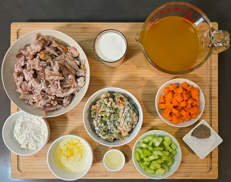 ingredients for the filling for a leftover turkey pot pie laid out on a cutting board: leftover turkey, cream, turkey stock, carrots, celery, green bean casserole, butter, oil, flour, salt and pepper