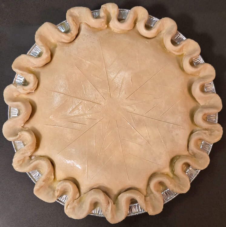 an overhead photo of a turkey pot pie with slashing in the shape of a snowflake before baking