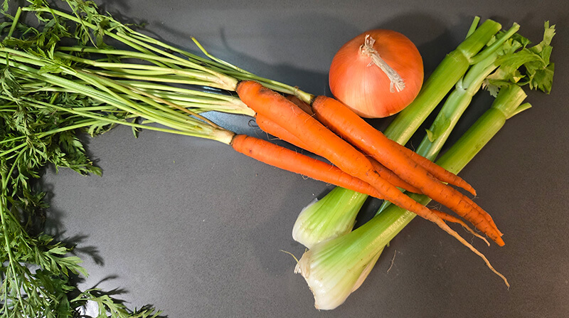 an overhead photo of vegetables: carrots with long green carrot tops, a sweet yellow onion, and three stalks of green celery