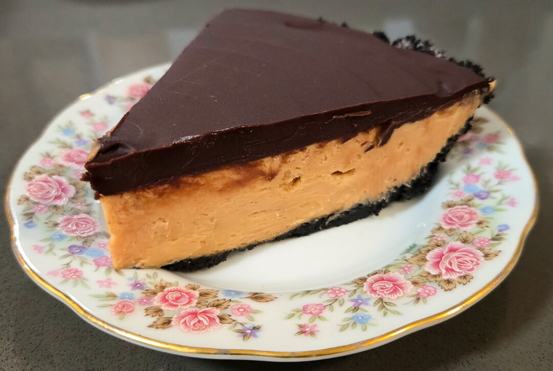 close up photo of a slice of no-bake peanut butter pie with a peanut butter cheesecake filling, an oreo cookie crumb crust, and a chocolate ganache topping