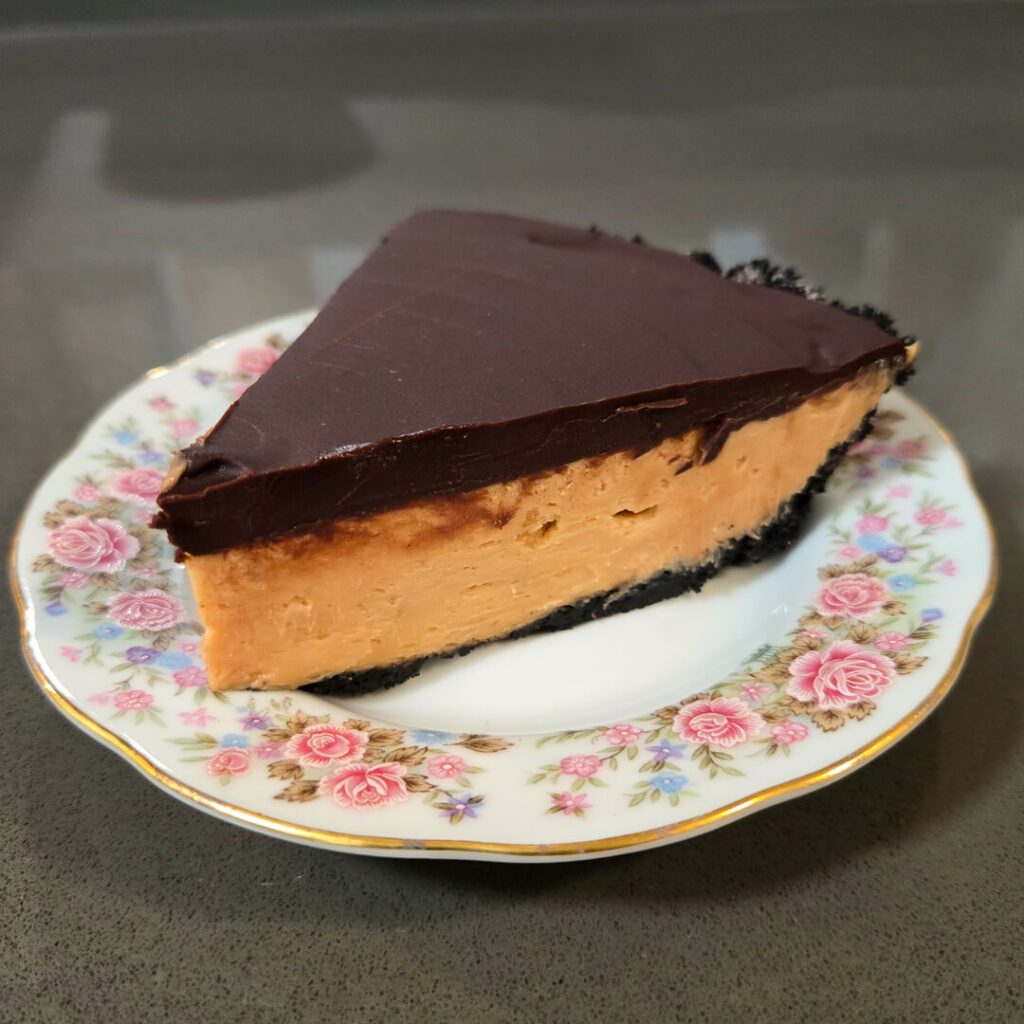 a slice of no bake peanut butter pie in an oreo crust with a ganache topping on a floral plate
