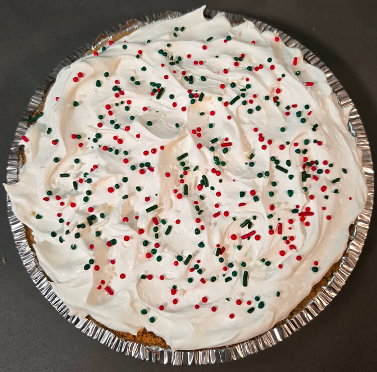 Overhead photo of a pie in graham cracker crust topped with Cool Whip and Christmas sprinkles