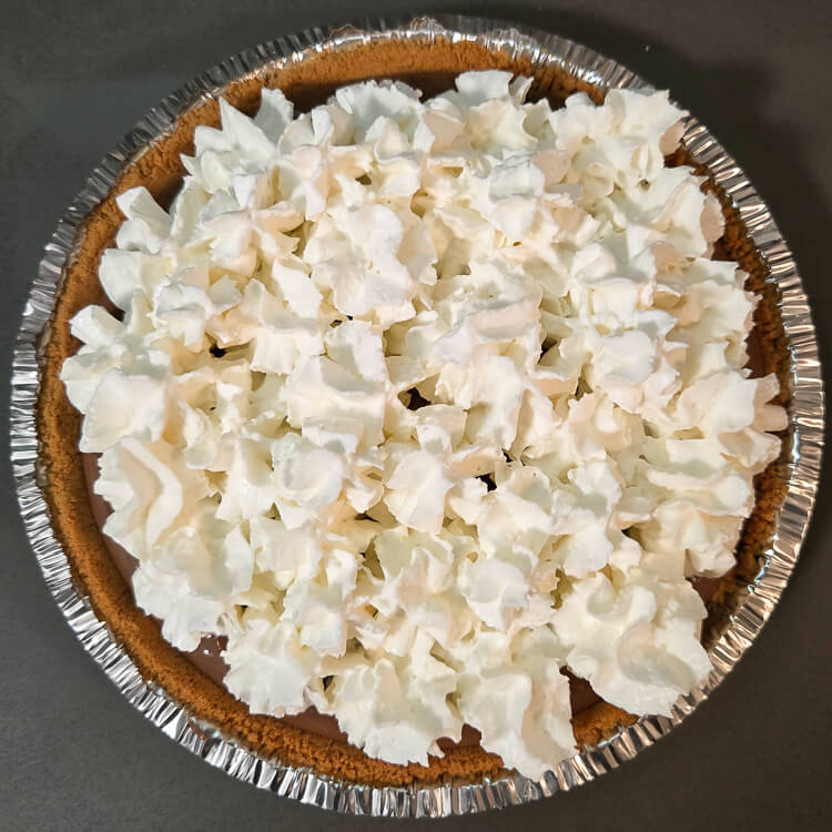 Overhead photo of a pie in a graham cracker crust topped with canned whipped cream