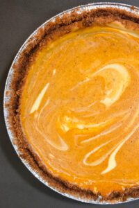 an overhead photo of a swirled pumpkin cheesecake pie in a graham cracker crust