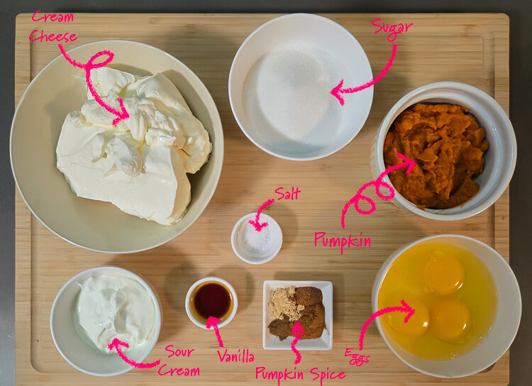 ingredients for a swirled pumpkin cheesecake pie: cream cheese, sugar, pumpkin puree, salt, sour cream, vanilla, pumpkin spice, and eggs