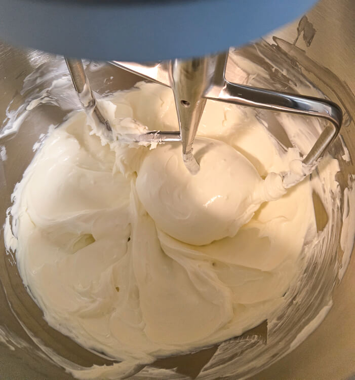 cream cheese and sour cream being mixed until smooth with no lumps in a stand mixer