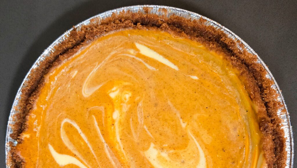 a horizontal overhead photo of half of a swirled pumpkin cheesecake pie in a graham cracker crust
