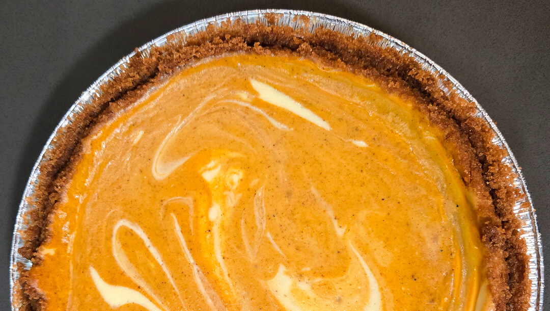 a horizontal overhead photo of half of a swirled pumpkin cheesecake pie in a graham cracker crust