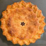 an overhead photo of a baked schnitz pie: a double crusted pie with a star cutout in the center baked to a golden brown color