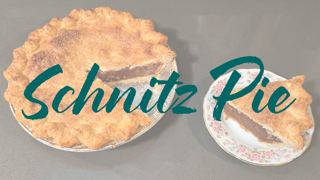 a landscape photo of a schnitz pie, with a slice cut out and placed on a plate next to it with a text overlay that reads "Schnitz Pie"