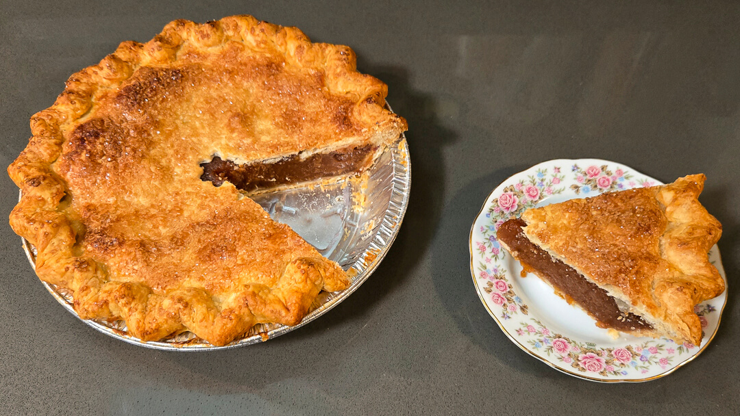 an overhead photo of an Amish apple schnitz pie with a slice cut out, and placed next to it on a floral plate