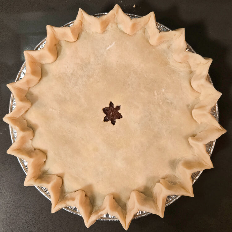 an overhead photo of an unbaked and unfinished double crusted pie. It has been crimped with pointed flutes and has a star cutout in the center